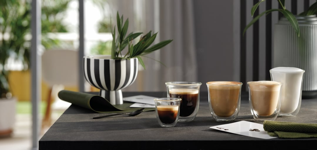 Various coffee drinks in glass cups on a dark table with a plant