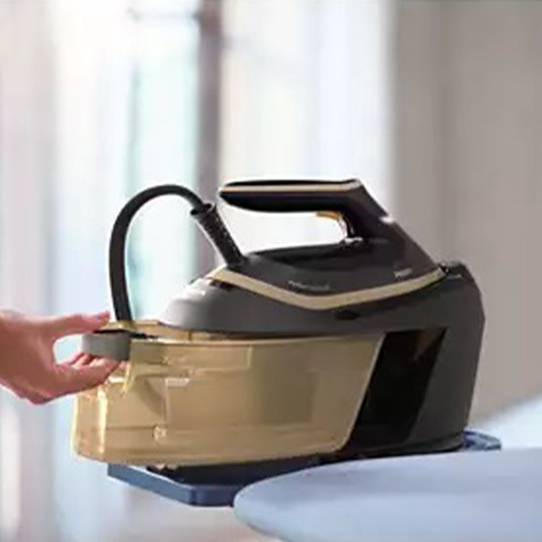 Hand removing the water tank from a Philips steam generator iron on an ironing board