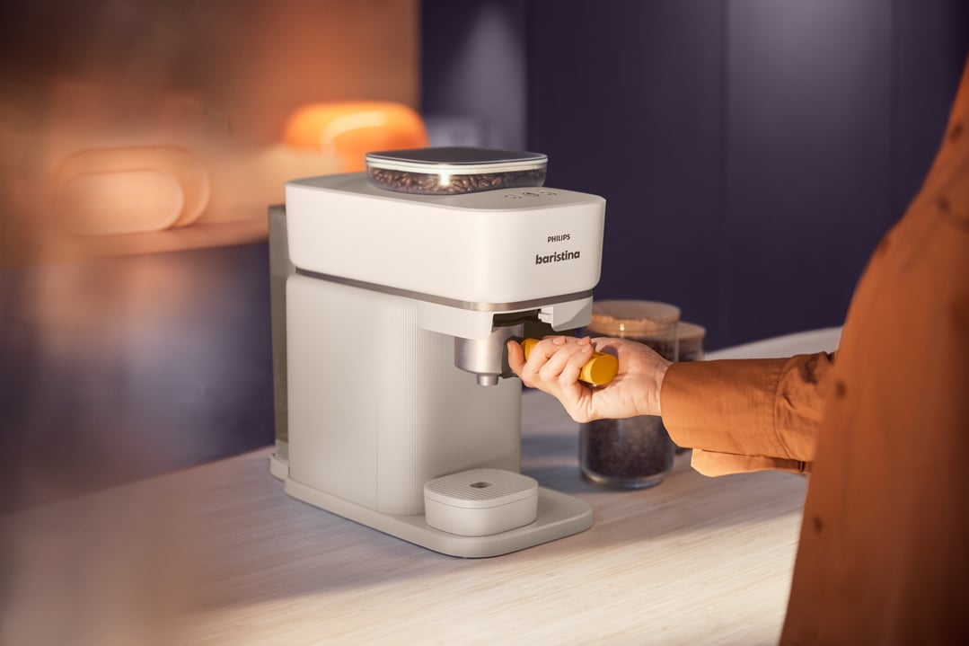 Person's hand inserting a yellow portafilter into a Philips Baristina coffee machine