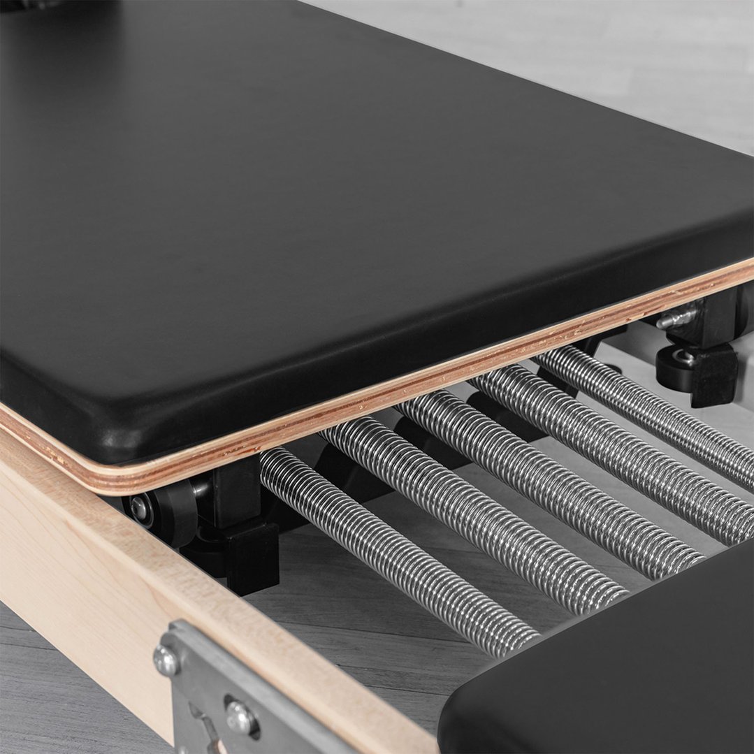 Close-up of the black padded carriage and springs of a Pilates reformer