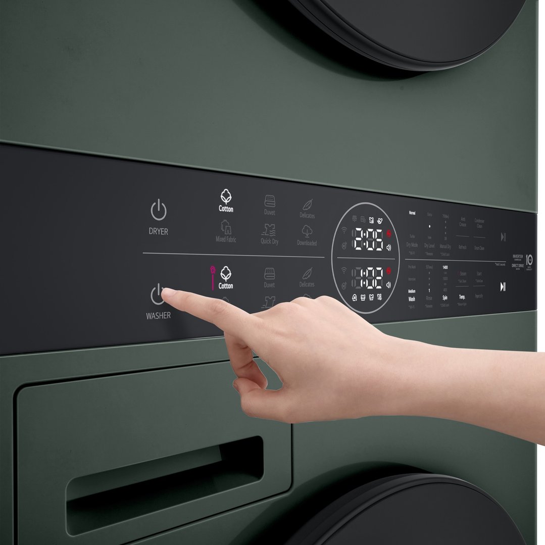 Hand pressing the washer power button on a green stacked washer dryer
