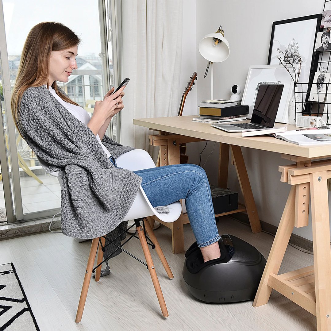 Woman using a black foot massager while sitting at a desk