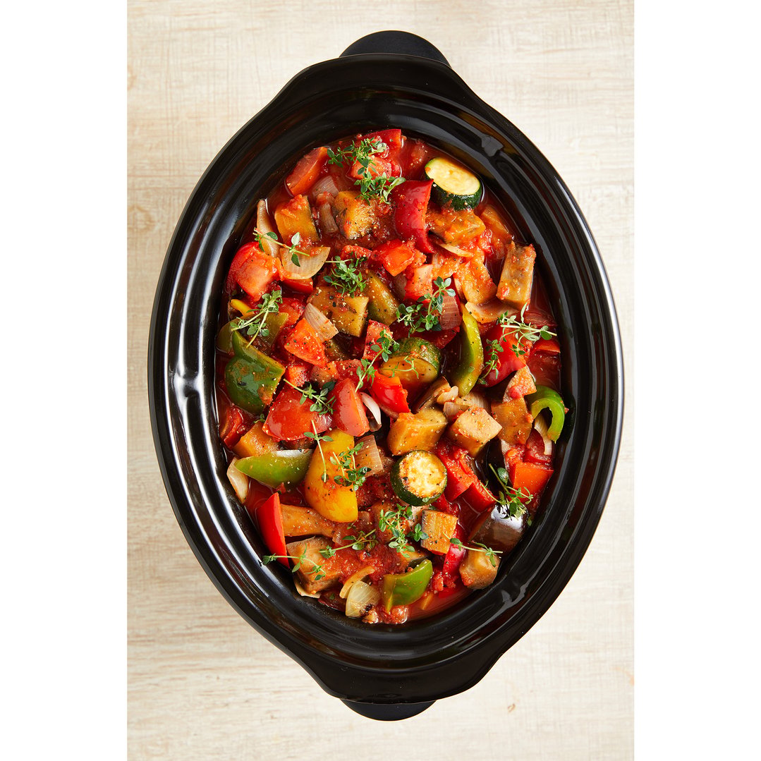 Overhead view of a slow cooker filled with ratatouille on a wooden surface