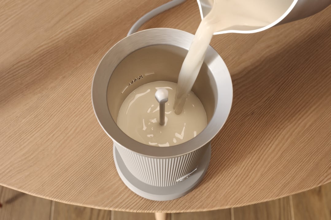 Milk being poured into a Baristina Milk Frother on a wooden table