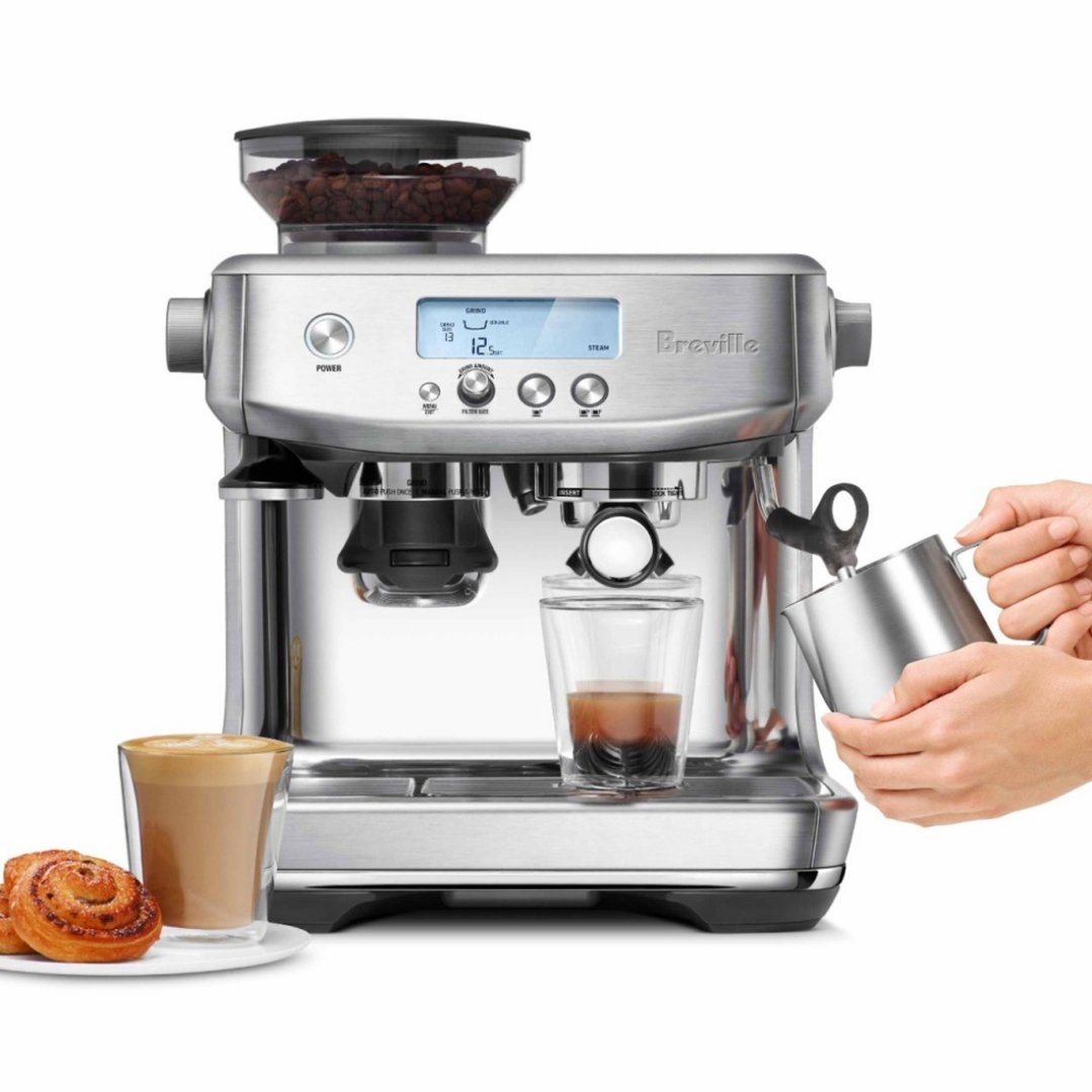 Hands pouring milk into a cup next to a Breville coffee machine