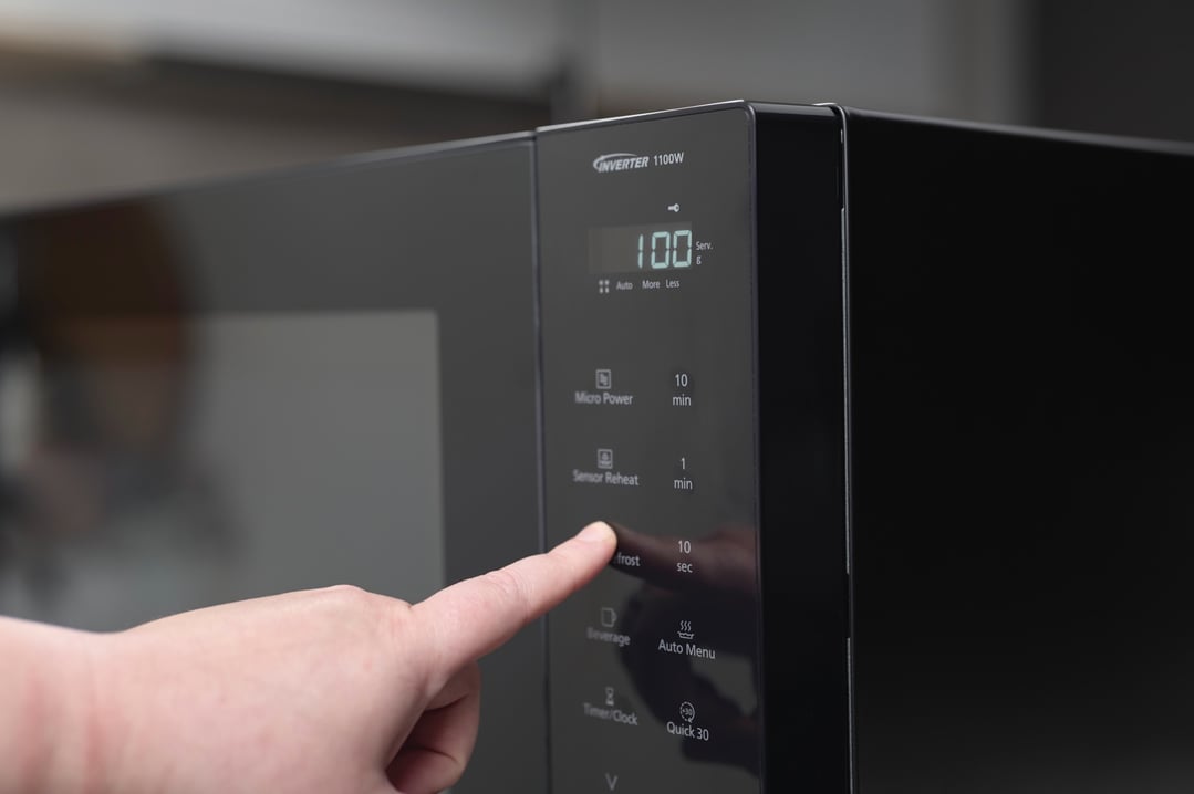 A hand pressing the defrost button on a black Panasonic microwave