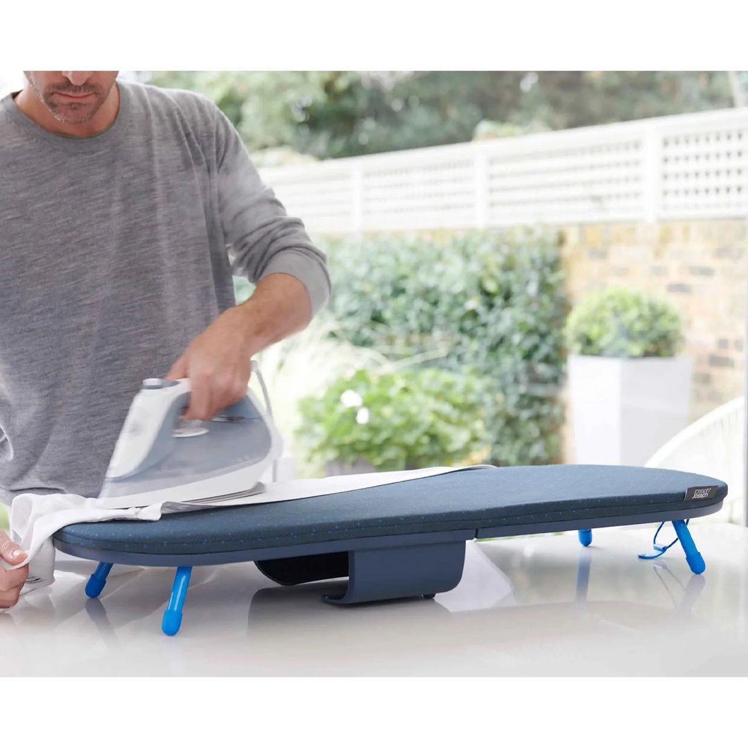 Man ironing a white shirt on a blue folding ironing board outdoors