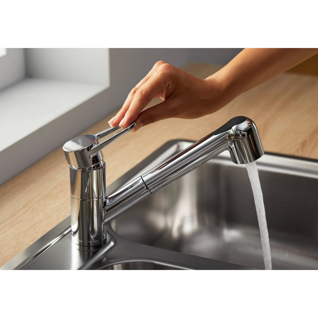 Hand operating a chrome tap with water flowing into a stainless steel sink