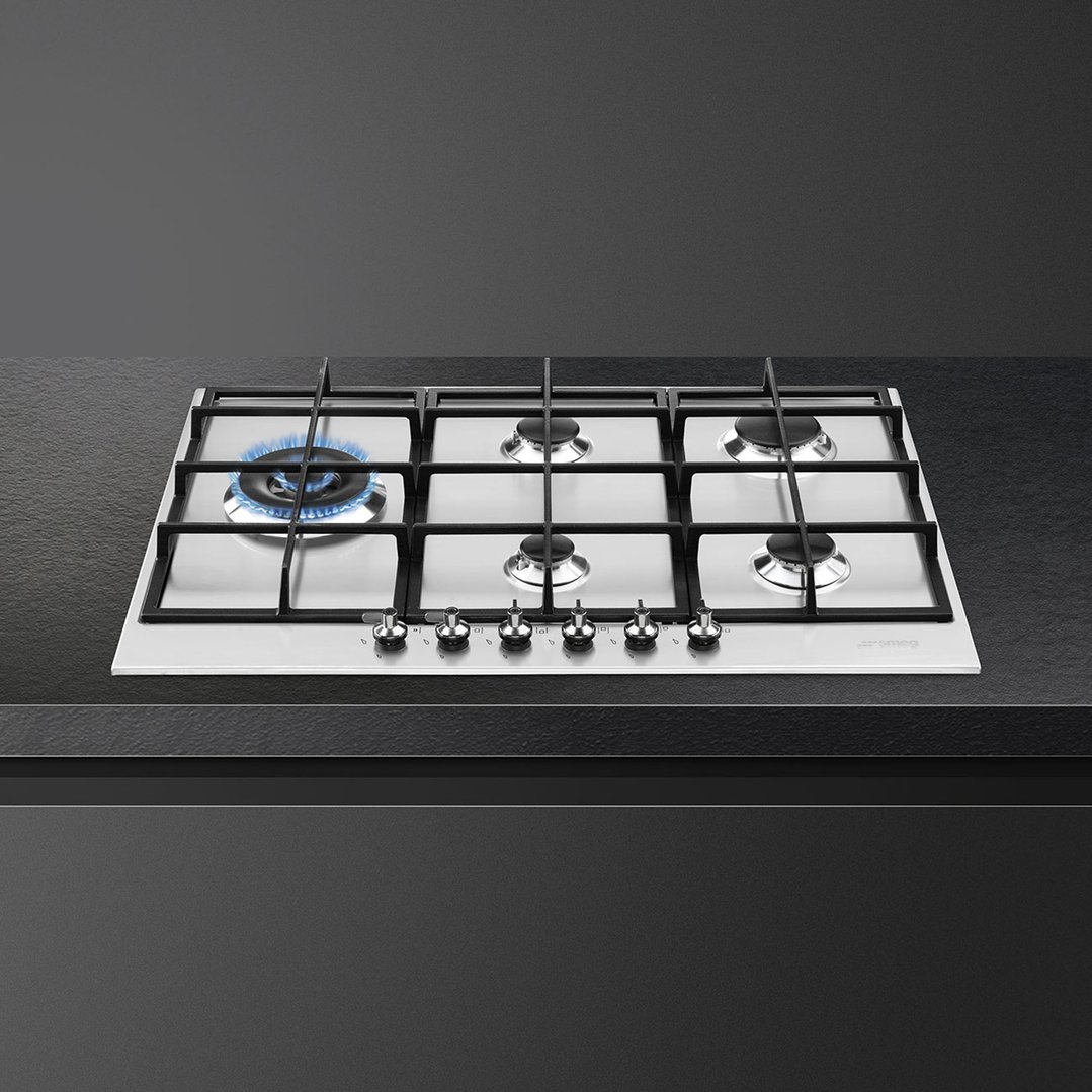 A stainless steel gas cooktop with one burner lit, on a dark countertop