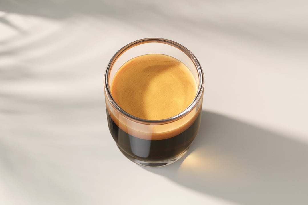 Espresso coffee in a clear glass on a light surface with shadows