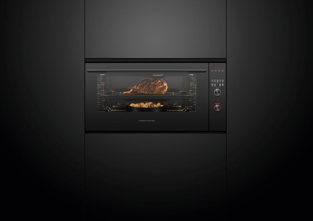 A black built-in oven with a large piece of meat and potatoes cooking inside