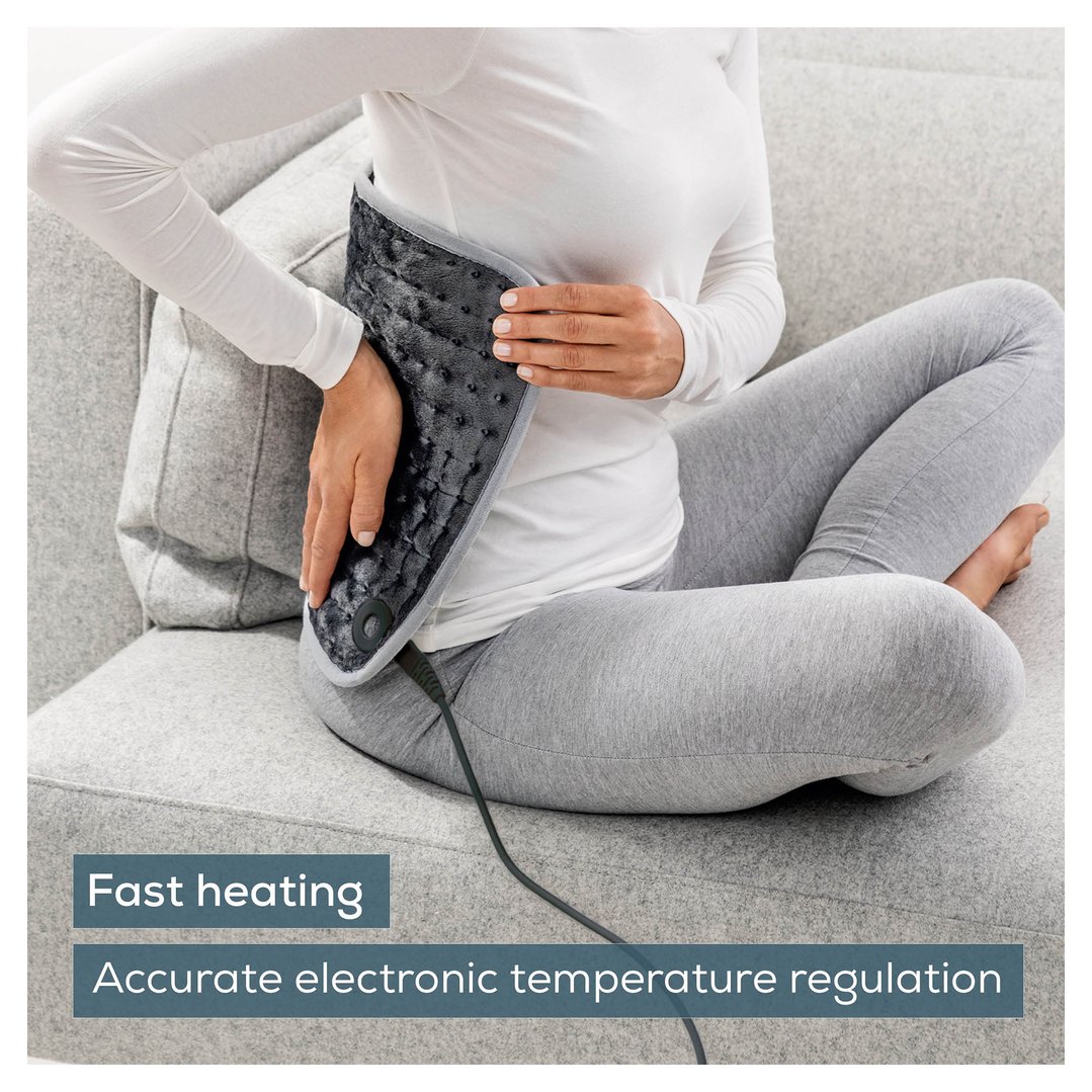 Woman sitting on a sofa using a personal heating pad on her lower back
