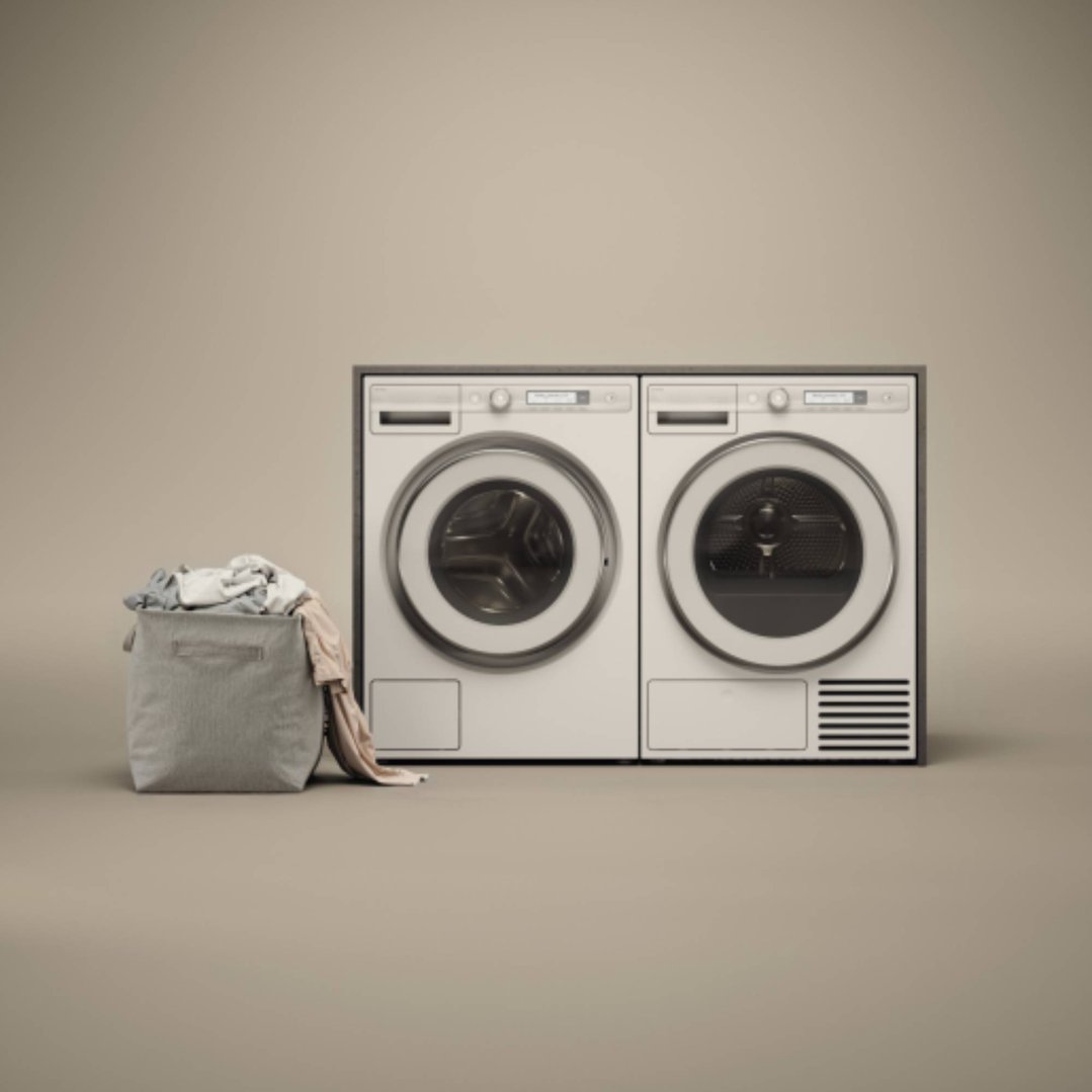 Two white washing machines next to a laundry basket with clothes