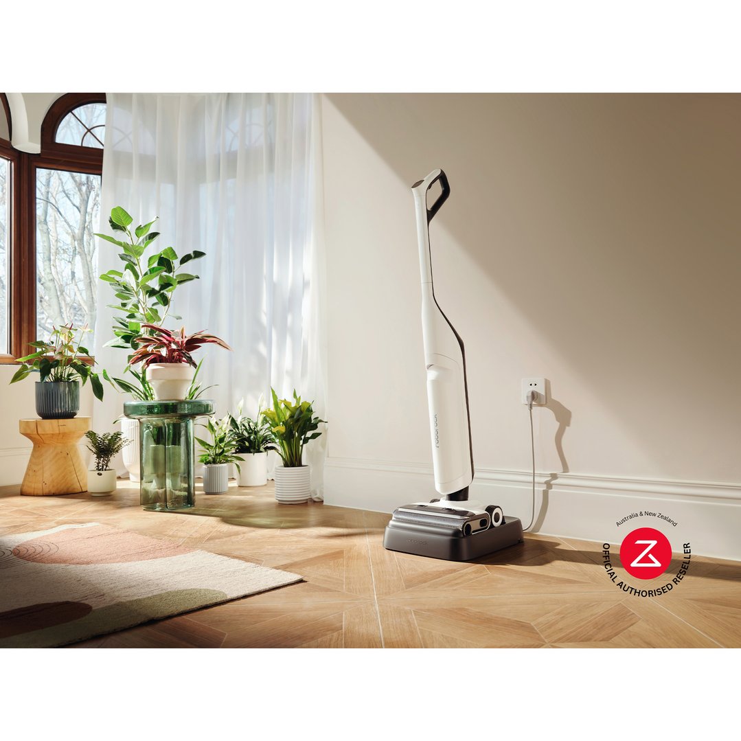 White Roborock vacuum cleaner charging in a bright room with many plants