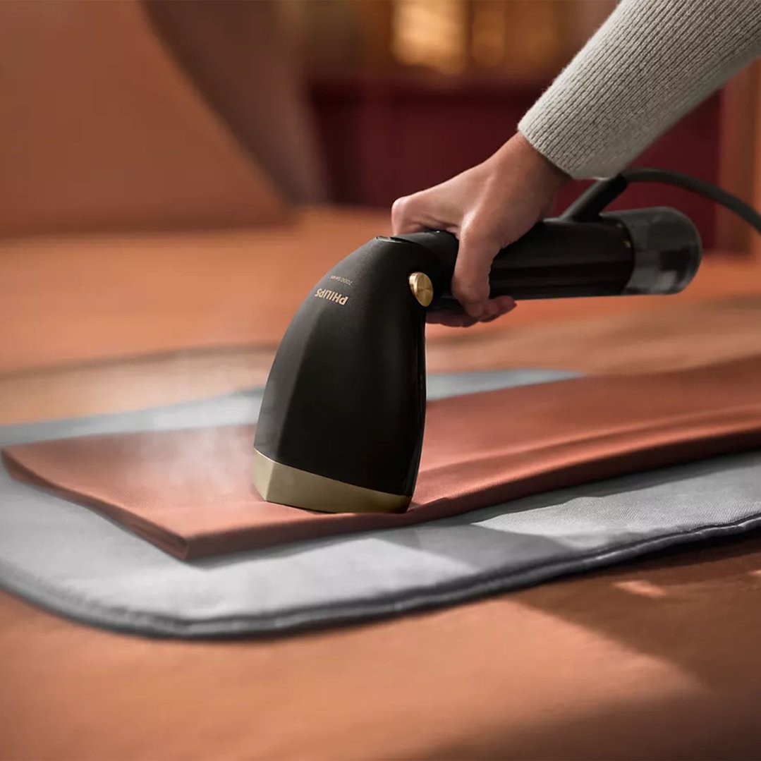 Handheld Garment Steamer steaming a brown garment on a grey mat