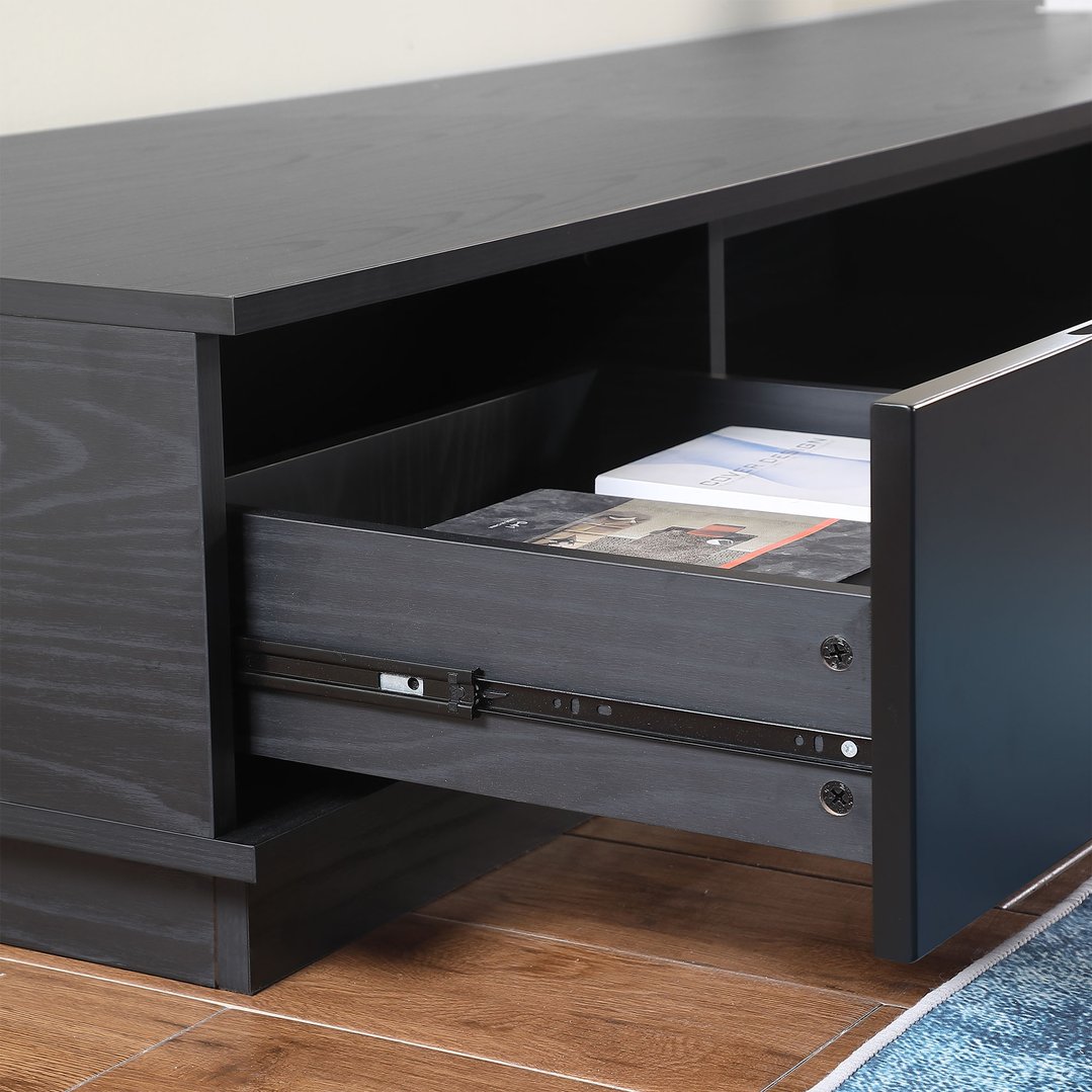 Close up of a black oak TV cabinet with an open drawer on a wooden floor
