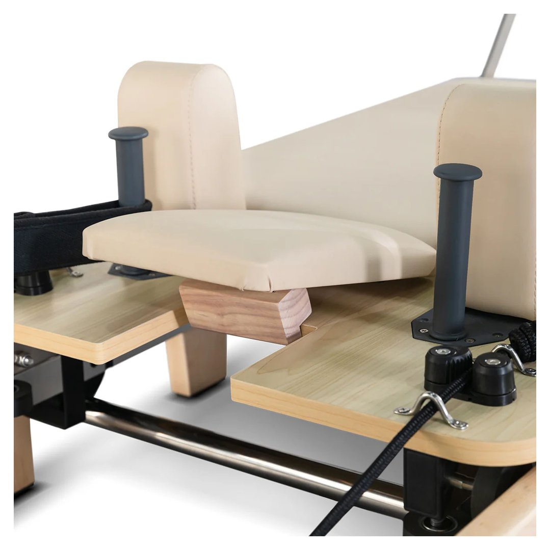 Close up of the beige padded seat and wooden frame of a pilates reformer