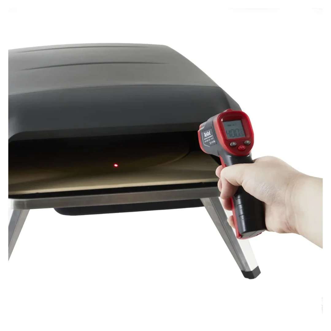 Hand holding an infrared thermometer, measuring temperature inside a pizza oven