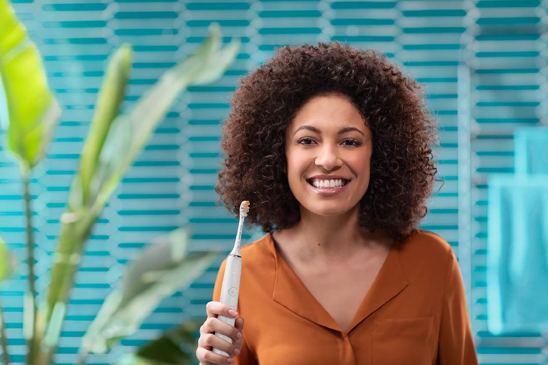 Smiling woman holding a Philips Sonicare DiamondClean 9000 electric toothbrush