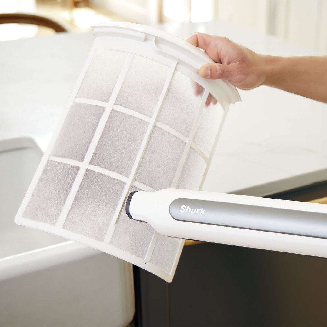 Hand using a Shark air purifier to clean a large white filter